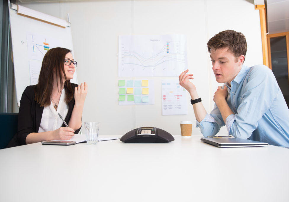 Young male and female business people using conference phone at desk in office